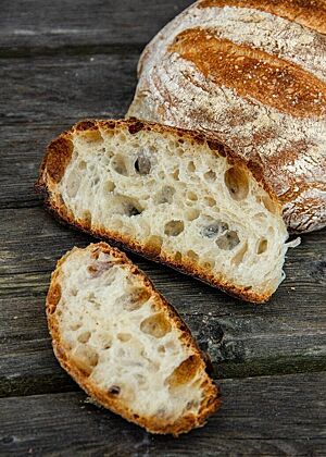 Ein offenporiges Brot im Anschnitt liegt auf einem verwitterten Holztisch.