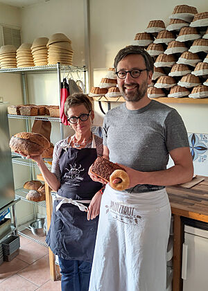 Angela und Lutz nach zwei Tagen Bäckereiberatung in ihrer Backstube. Angela Nöthlings hält ein Bloomer, Lutz Geißler ein Schwarzbrot und einen Bagel in der Hand.