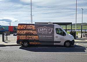 Ein Transporter vom SuperValue-Supermarkt in Dingle, auf dem für die Handwerksbäckerei im Laden geworben wird. Ein mit einem Brotfoto beklebter Transporter steht am Hafen von Dingle.