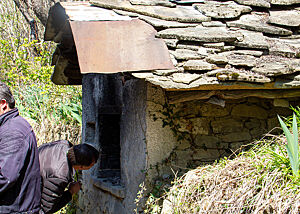 Ein alter, rustikal gemauerter Backofen hat Steinplatten als Dacheindeckung.