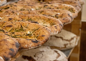 Eine Art Focaccia. Die Focaccia sind mit Rosmarinnadeln und Knoblauchzehen bestreut und glänzen von Olivenöl.