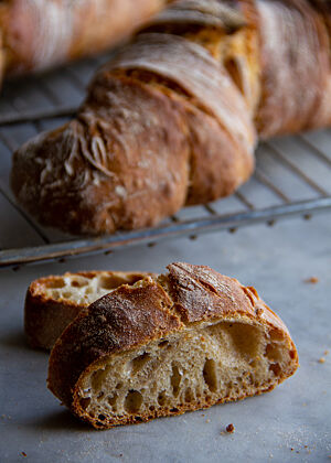 Dinkel-Emmer-Wurzeln: Brote, wie dieses Dinkel-Emmer-Brot, brauchen gut entwickelte Teige. Eine Knetmaschine hilft dabei. An einer Scheibe des Wurzelbrotes lässt sich gut die grobporige, mittelbraune Krume und die dünne, knusprige Kruste mit rustikalem Ausbund sehen.