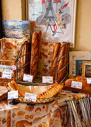 Ein Drahtkorb mit senkrecht stehenden Baguettes auf einem Tisch in einer Ecke des Ladens.