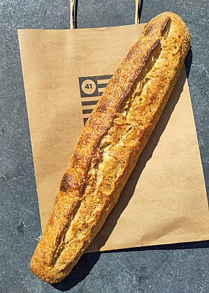 Das Baguette von Bread 41 hat einen höheren Schalenanteil als die Vergleichsbaguettes in Dublin und ist insgesamt kompakter und säuerlicher. Ein goldbraunes Baguette liegt auf der Papiertüte von Bread 41.