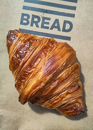 Das Croissant von Bread 41 – gut, aber nicht so gut wie in der Russell Street Bakery. Ein dunkelbraunes, glänzendes Croissant auf einer Papiertüte mit Aufdruck „Bread 41“.