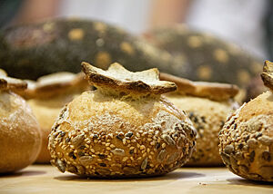 Brötchen mit Krone. Das in Saaten gewälzte Brötchen wurde auf der Oberfläche mit einem Sternmuster eingeschnitten, sodass sich die Kruste während des Backens als eine Art Krone nach oben gebogen hat.