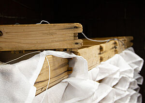 Mit weißen Tüchern ausgelegte, bereinandergestapelte Holzkästen. In einem Kasten ist Reis zu sehen.