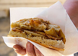 Eine Hand hält ein Fladenbrot, der mit gebratenem Strudelteig gefüllt ist.