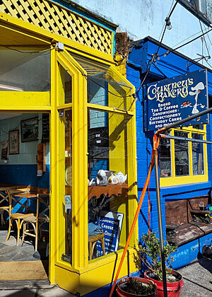 Courtney's Bakery in Dingle. Blaue Fassade mit gelbem Eingangsbereich. Die Bäckerei hat eher klassische Ware mit Backmitteleinsatz im Angebot.
