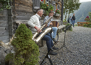 Peter Zulauf und sein Kollege sitzen vor einer Almhütte und spielen Saxophon und Akkordeon.