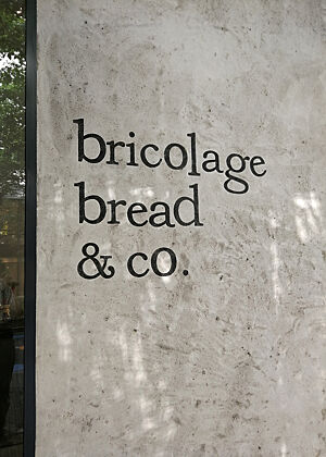 Eine damals kaum eine Woche alte Bäckerei. Schwarze Schrift auf rauem Beton zeigt den Namen einer japanischen Bäckerei: „bricolage bread & co.“