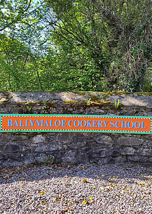 Der Eingang zur Ballymaloe Cookery School in Ballymaloe. Ein farbenfrohes Schild mit der Aufschrift "Ballymaloe Cookery School".