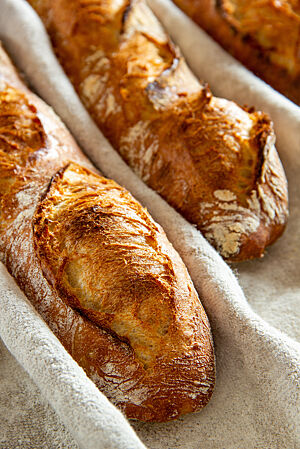 Kräftig ausgebackene, rustikal aufgerissene Baguettes im gestaubten Leinen.