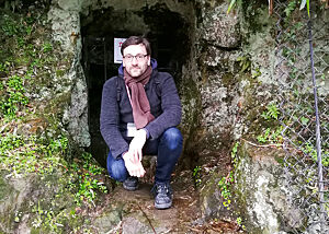 Lutz Geißler hockt vor einem verschlossenen Höhleneingang.
