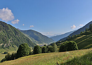Links und rechts des grünen Tals erheben sich waldbewachsene Berge.