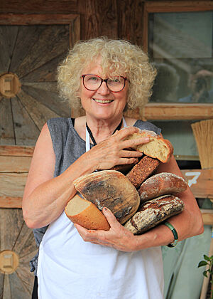 Mit mehreren Broten im Arm steht Roswitha Huber vor der Almhütte.