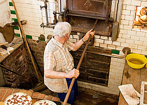 Ein Bäcker schiebt mit einem Holzschieber Kuchen in den Ofen.