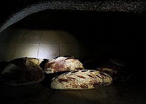 Darunter klassische San Francisco Sourdough Breads. Im dunklen Ofen sind mehrere bemehlte Brotlaibe zu sehen.