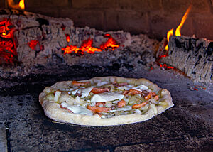 Die Lachspizza liegt im Holzofen in der Nähe der Glut.