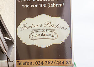 Immer eine Reise und Verkostung wert: Fischers Bäckerei „anno dazumal“ in Kühnitzsch. Auf einem Außenreklame-Schild stehen Name und Telefonnummer der Bäckerei Fischer.