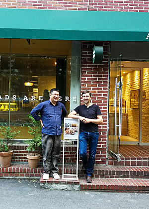 Herr Mo und Lutz Geißler stehen vor der Fassade seiner ersten Bäckerei.