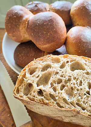 Röggelchen und Bloomer. Das Weizensauerteigbrot mit lockerer, saftiger Krume liegt vor einem Teller mit Röggelchen.