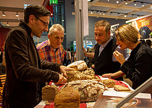 Lutz Geißler im Gespräch u.a. mit Stevan Paul (2.von rechts) und Daniela Haug (Autoren und Fotografen des Buchs „Auf die Hand“) bei der Brotverkostung. Stevan Paul und Daniela Haug besuchen den Messestand von Lutz Geißler und begutachten das von ihm angebotene Brot.