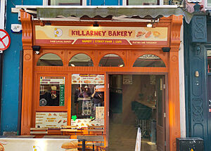 Die Killarney Bakery von der Straße aus gesehen. Sie ist eine von nur sehr wenigen Bäckereien in der Stadt. Ein auffälliges Haus mit blauem Anstrich und orange-farbiger Bäckerei-Front.