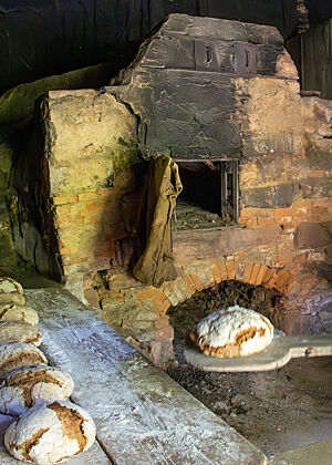 Ein Brot liegt auf dem Schieber, während lange Reihen fertiger Laibe zum Abkühlen auf Holzbrettern liegen.