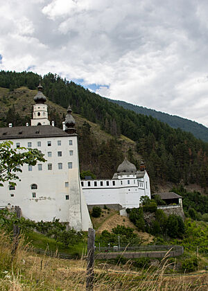 Das große weiße Gebäude des Stift Marienberg erhebt sich imposant am bewaldeten Berghang.
