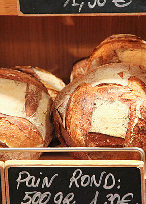 Goldbraun ausgebackene Weizenbrote mit rustikal aufgerissenen, quadratischen Einschnitten liegen in der Auslage einer französischen Bäckerei.