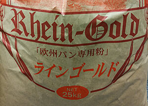 Deutsches Mehl neu verpackt und benannt. Ein Mehlsack tragt die altdeutsche Aufschrift „Rhein-Gold 25 kg“ sowie japanische Schriftzeichen.