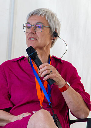 Christa Lutum Prof. Cecarelli sitzt auf einem Stuhl und spricht ins Mikrofon.