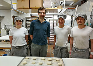 Lutz Geißler steht mit drei japanischen Bäckern in der Backstube der Bäckerei „Tanne“.