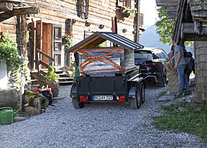 Ein Auto mit Anhänger transportiert einen mobilen Holzbackofen.