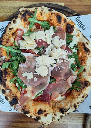 48 Stunden lang geführter Pizzateig, im Holzofen gebacken. Gegessen bei Tango Streetfood in Killarney. Mit Rucola, Schinken und Käse belegte Pizza mit dickem und dunklem Rand.