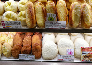 Panierte und frittierte Köstlichkeiten aus „Berliner-Teig“ gefüllt mit Currymixturen (unten links in Braun). Im Regal einer japanischen Bäckerei liegt paniertes und frittiertes Feingebäck in unterschiedlichen Farben und Formen.