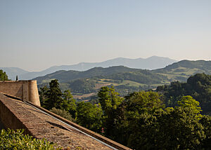 Blick von Urbinos Festung ins Grün. Über den Festungswall aus Backstein sieht man bis zum Horizont grüne Hügel mit Wäldern und Weinbergen.