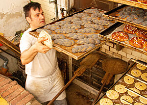 Ein Bäcker stellt das Blech mit den frisch gebackenen Mohnzöpfen in ein Regal zum Auskühlen.