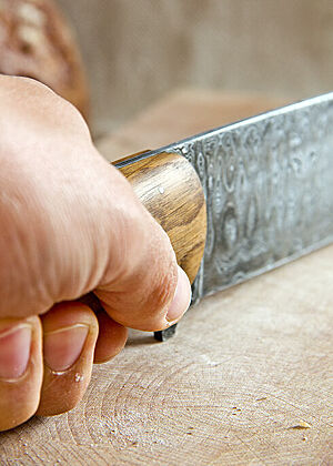 Eine Hand umfasst den Holzgriff des Damast-Brotmessers.