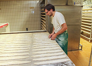 Lutz Geißler steht vor einem Abziehapparat mit Unmengen von Baguettes, die eingeschnitten werden müssen.