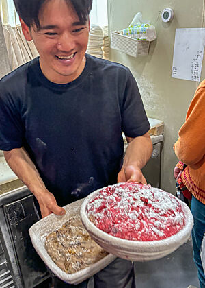 Der Bäcker hält in jeder Hand einen Gärkorb mit einem hellbraunen und einem rosafarbigen Teig.