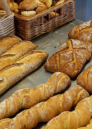 Baguettes und Wurzelbrote liegen neben Weizenbroten auf der Arbeitsfläche.