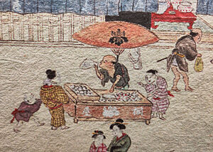 Ein Ausschnitt aus einem alten Bild Tokyos, dessen Original sich in Berlin befindet. Hier ist ein Verkäufer des wohl ersten Brotes auf japanischem Boden zu sehen: Manju. Es stammt aus China. Rundgeschliffene und gefüllte Weizenteiglinge werden gedämpft. Der Händler bläst gerade eine Tüte auf, um Manjus zu verpacken.