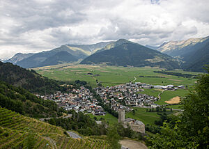 Blick vom Kloster Marienberg nach Plawenn. Das Örtchen Plawenn liegt in einem weiten, grünen Tal, umgeben von bewaldeten Bergen. Im Vordergrund ziehen sich Weinreben den Hanghinunter zu einer mittelalterlichen Burg.