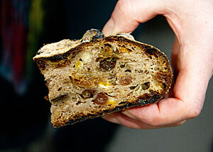 Früchtebrot mit TA 225 Eine Hand hält ein Stück Früchtebrot in der Hand. Zu sehen ist die feuchte Krume, in der Rosinen, Nüsse und Feigen schwimmen.