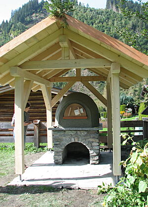 Ein neu gebauter Lehmbackofen steht geschützt unter einem Holzdach.