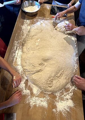 Auf der Arbeitsfläche liegt eine große Menge Teig. Es ist der Inhalt einer Teigwanne, was einem Viertel der hergestellten Gesamtteigmenge entspricht.