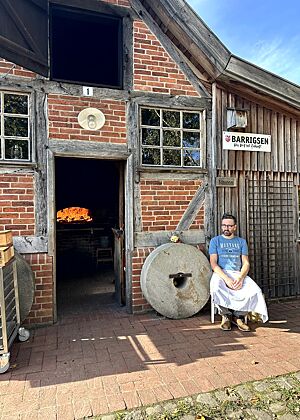 Lutz sitzt im Schatten vor dem Backhaus auf einem Stuhl.