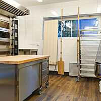 Blick in eine professionelle Backstube mit Teigkneter, Arbeitsplatte, Bäckerei-Ofen und verschiedenen Arbeitsutensilien 